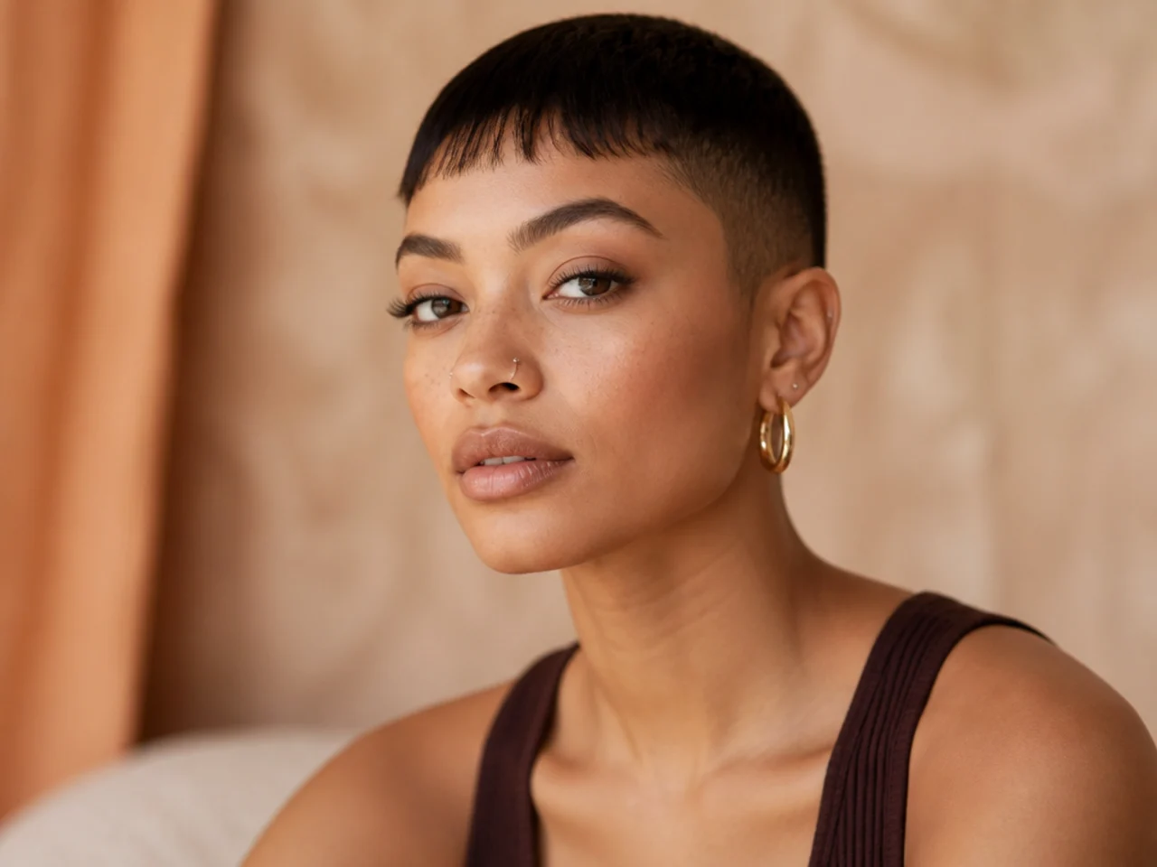 realistic photo of a feminine buzz cut featuring added bangs, dark brown hair, round face, soft feminine lines