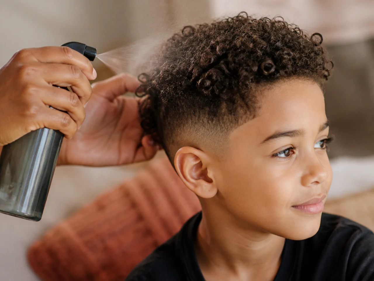 A parent refreshing a boy's curls with a water spray