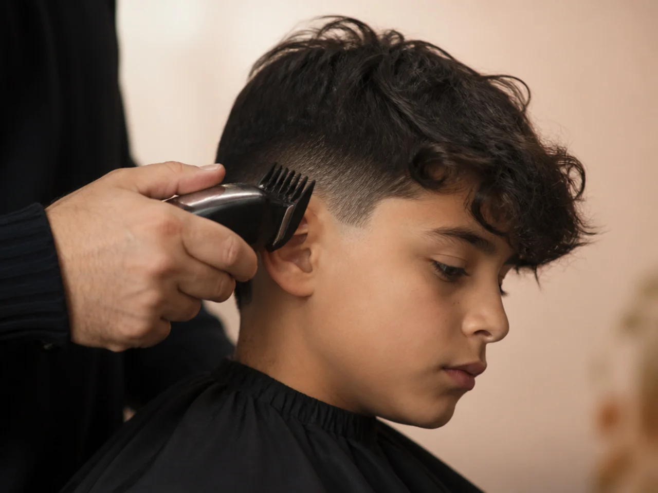 Clippers running a medium guard along the side of a boy's head above longer hair