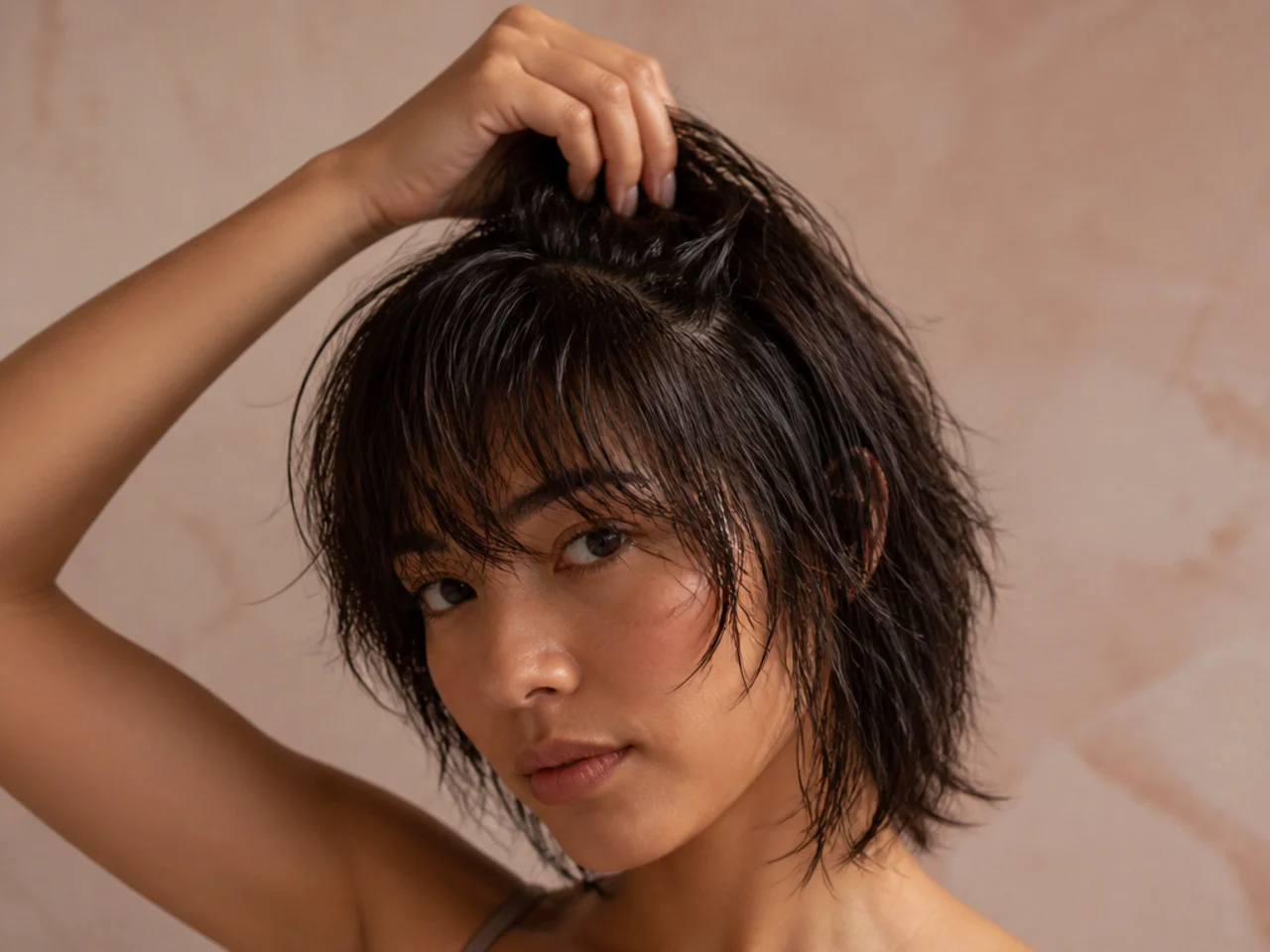 Fingers lifting damp roots at the crown of a shag haircut