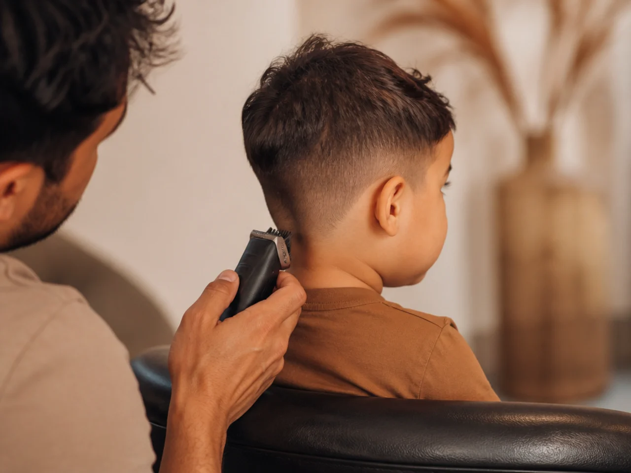 A parent holding a cordless trimmer beside a seated toddler