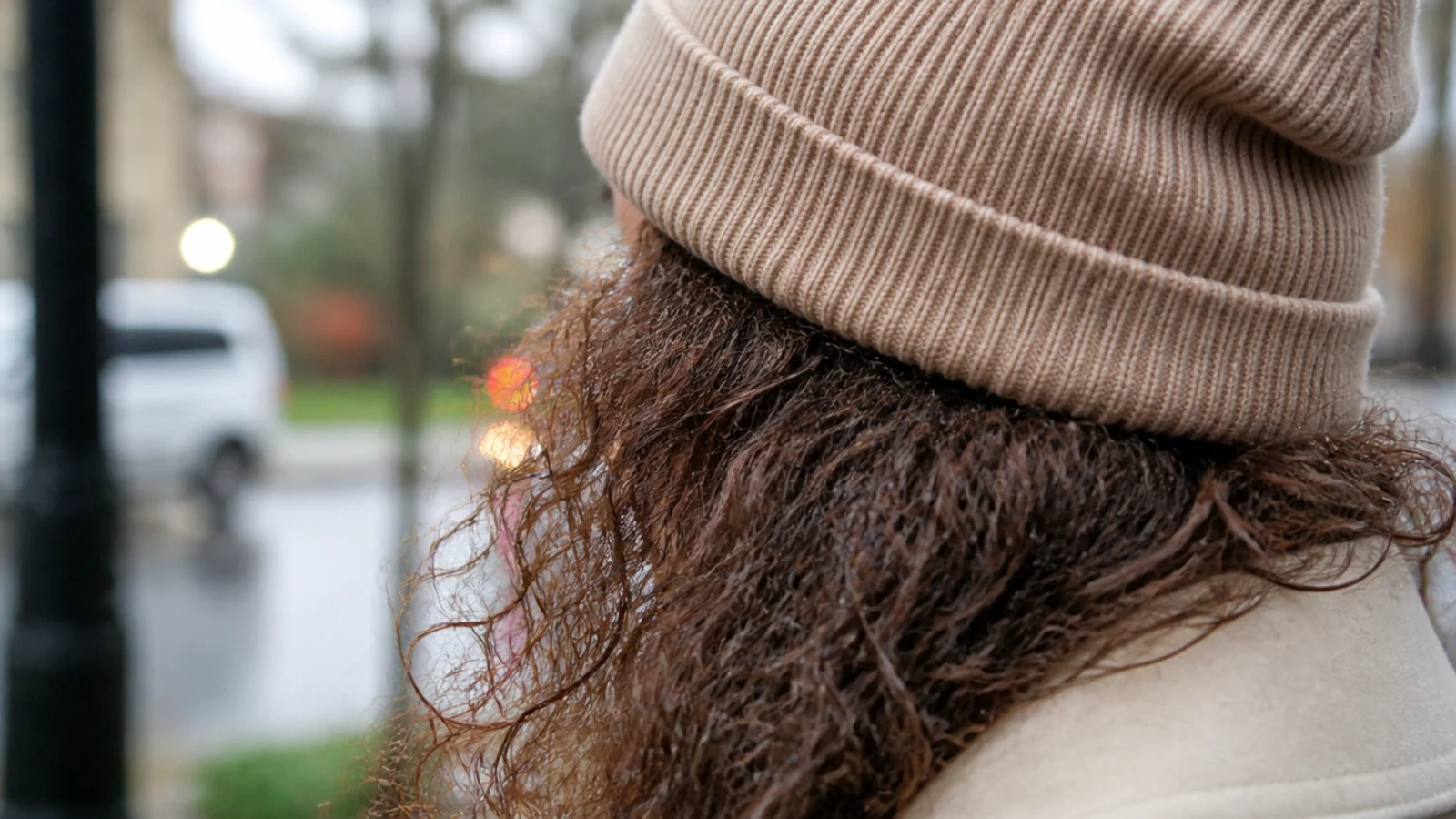 Curls falling out from under a knitted beanie on a grey day