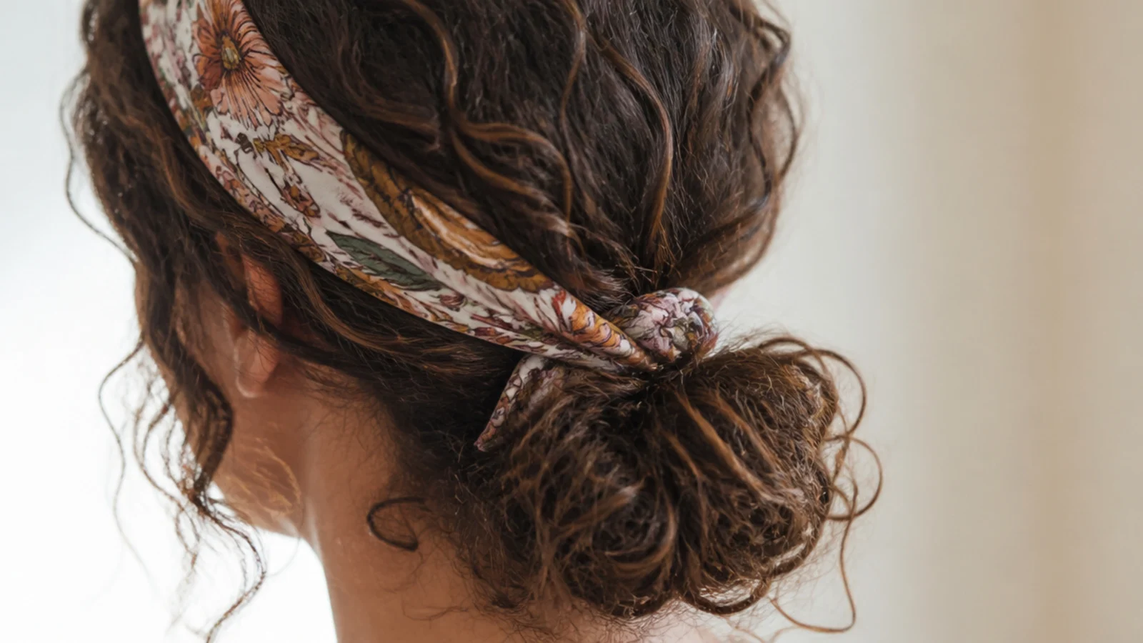 A low curly bun finished with a patterned silk scarf at the hairline