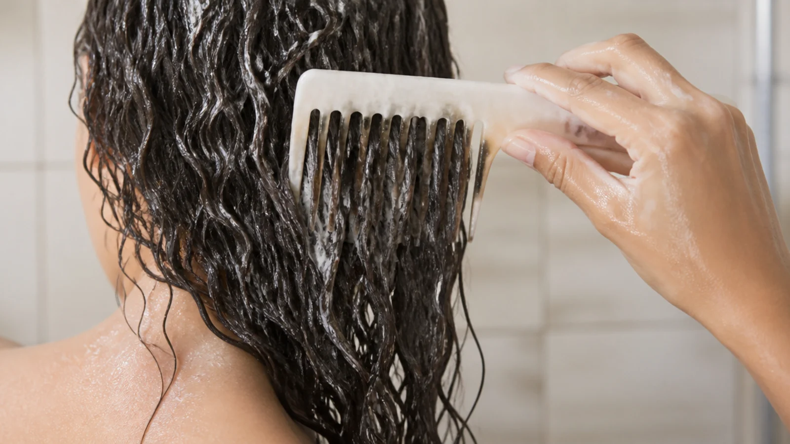 A wide tooth comb drawn through conditioner coated hair