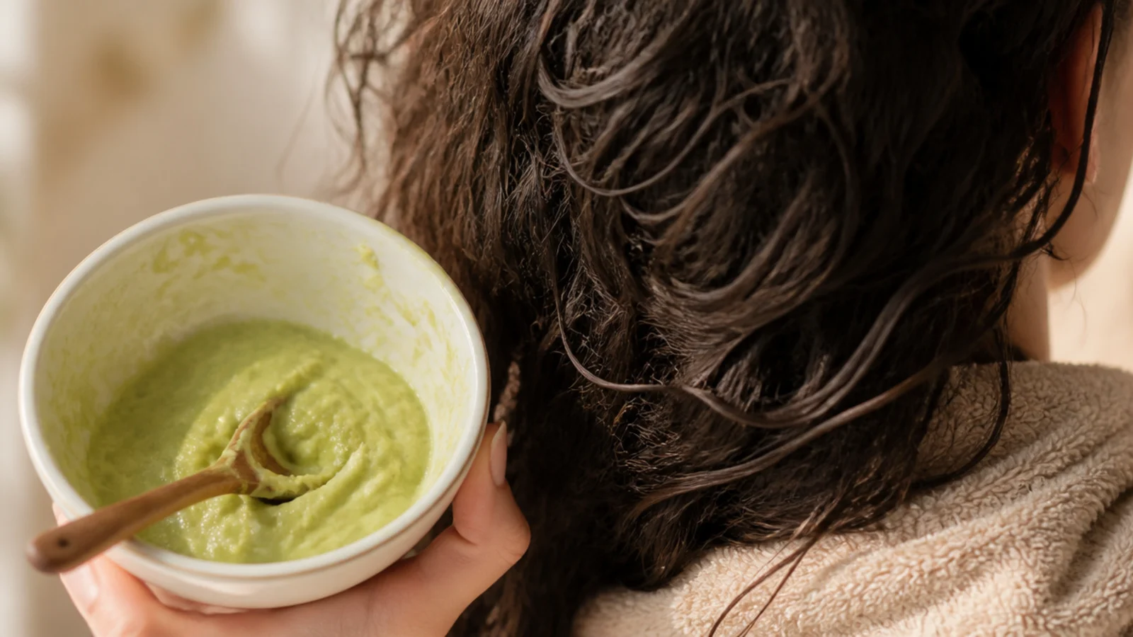 Mashed avocado in a bowl beside a jar of coconut oil and a spoon