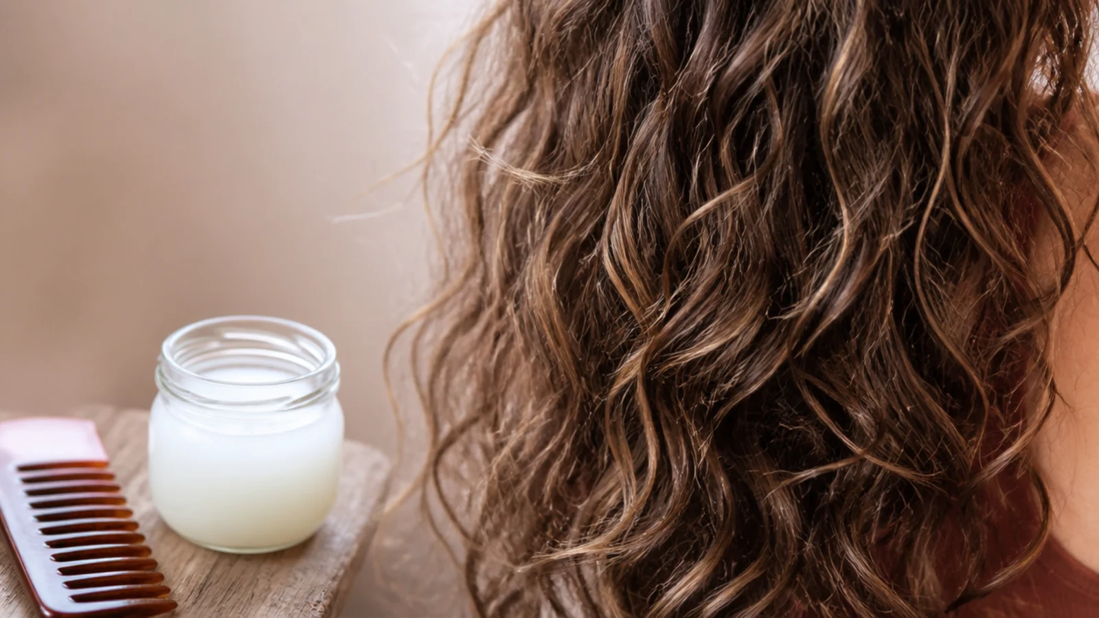 Solid white coconut oil in an open glass jar next to a wide tooth comb