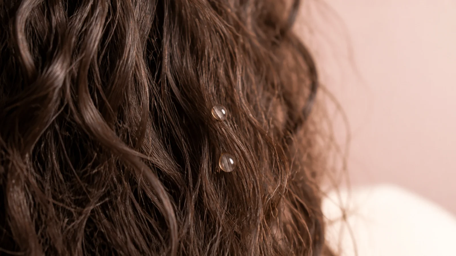 A few drops of clear serum being rubbed between two palms above dried hair