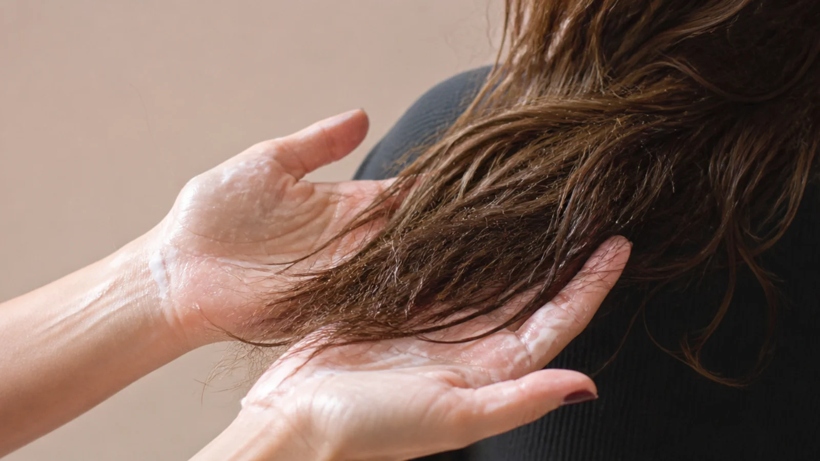 Hands smoothing the last of a cream over the ends of hair held forward over the shoulder