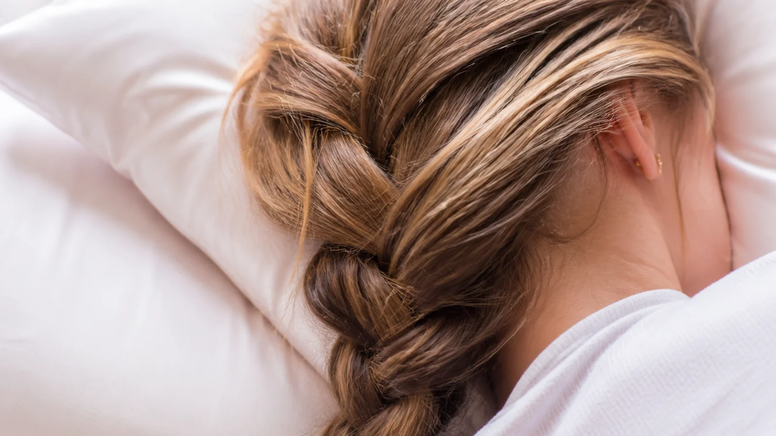 A loose braid resting on a silk pillowcase in dim bedroom light