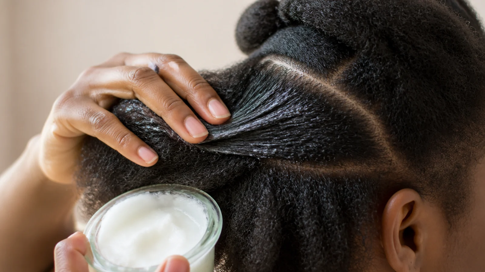 Oil poured into a palm beside dry sectioned hair
