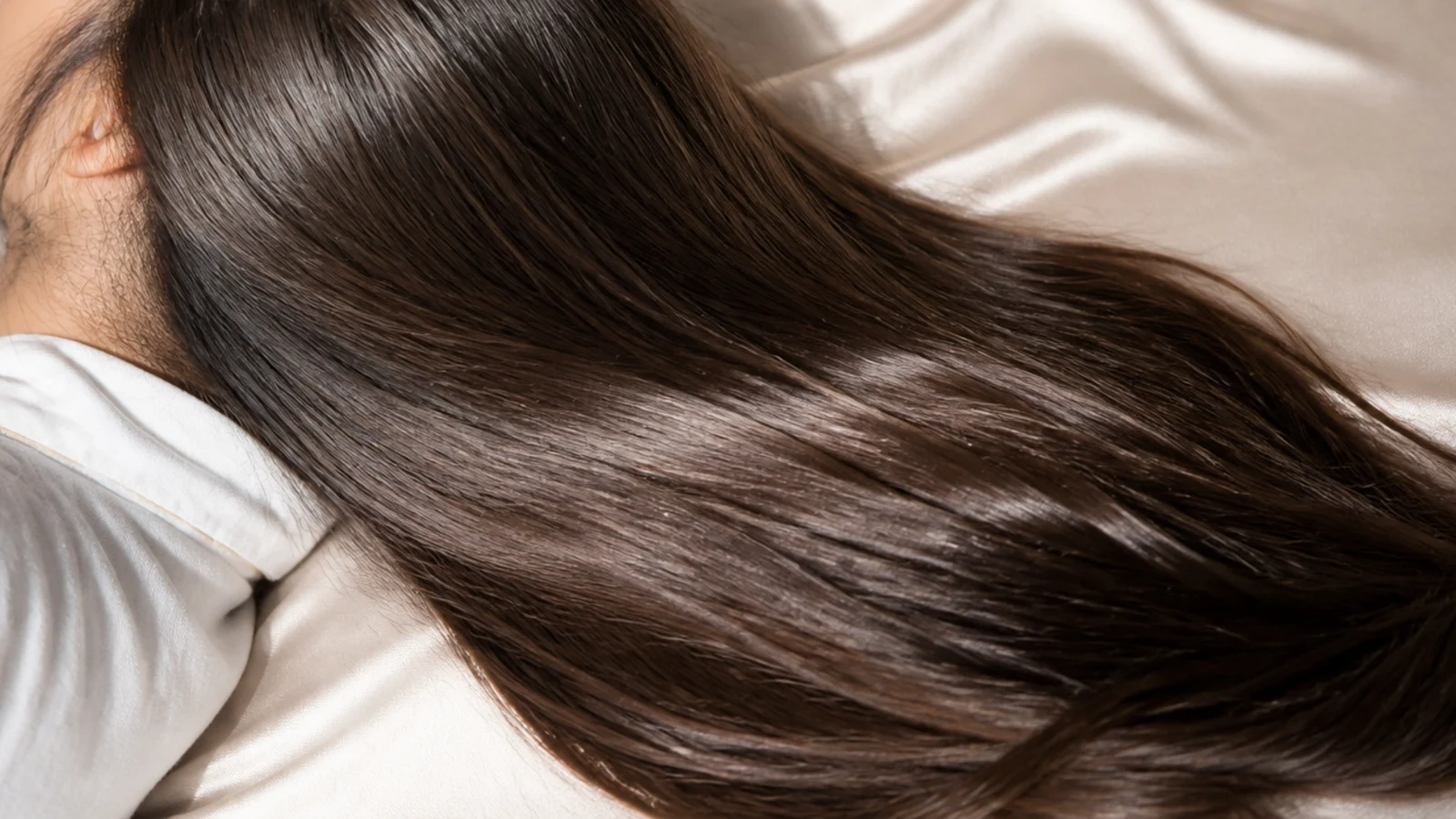 Hair lying across a satin pillowcase on a made bed