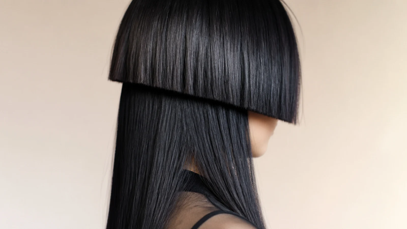 A hard edged dark bowl shape cut straight across the temples against a plain wall